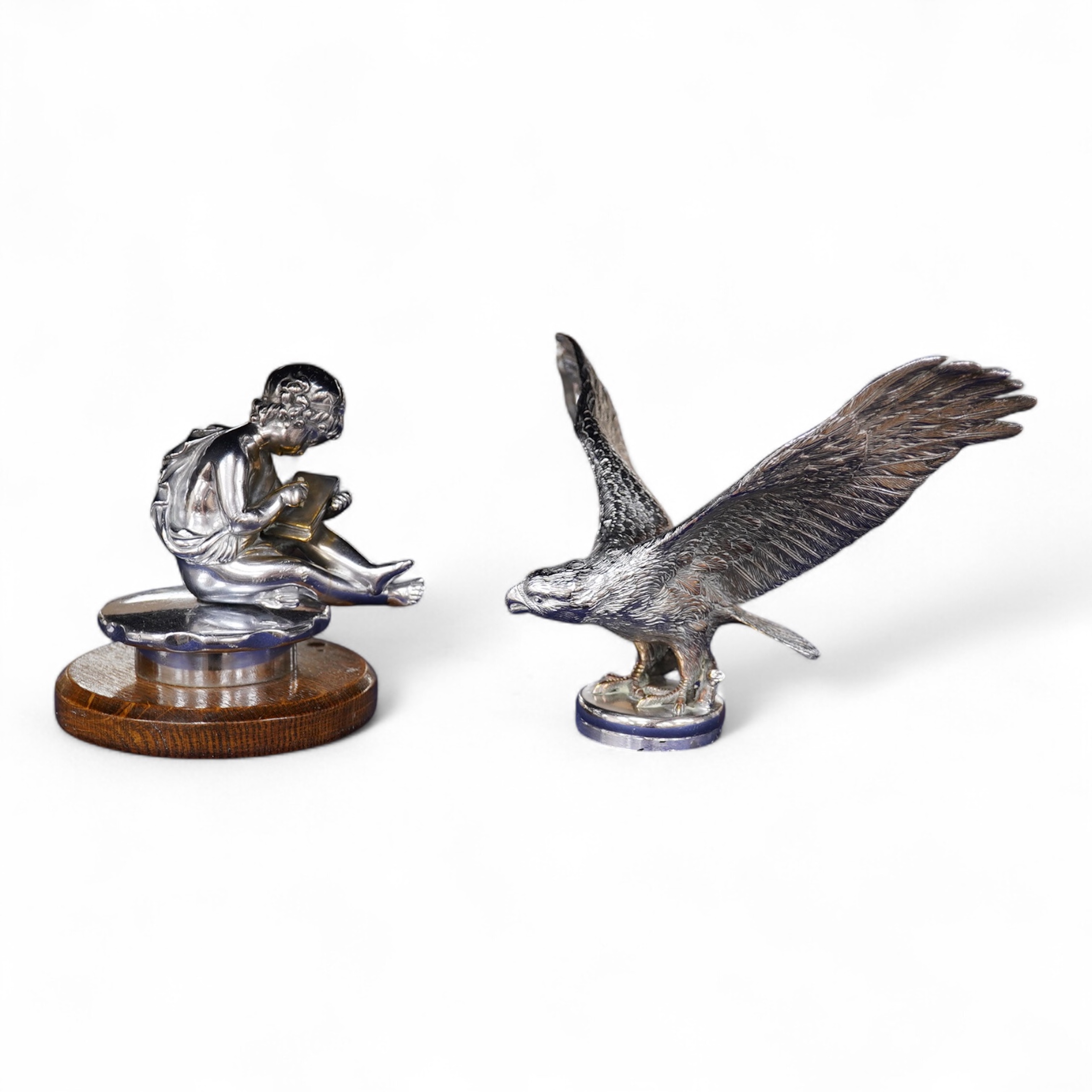 Two chrome car mascots, one in the form of an eagle stamped Finnigans London, wingspan 26cm, and the other of a classical child writing, mounted on a substantial radiator cap and oak base. Condition - fair to good, some